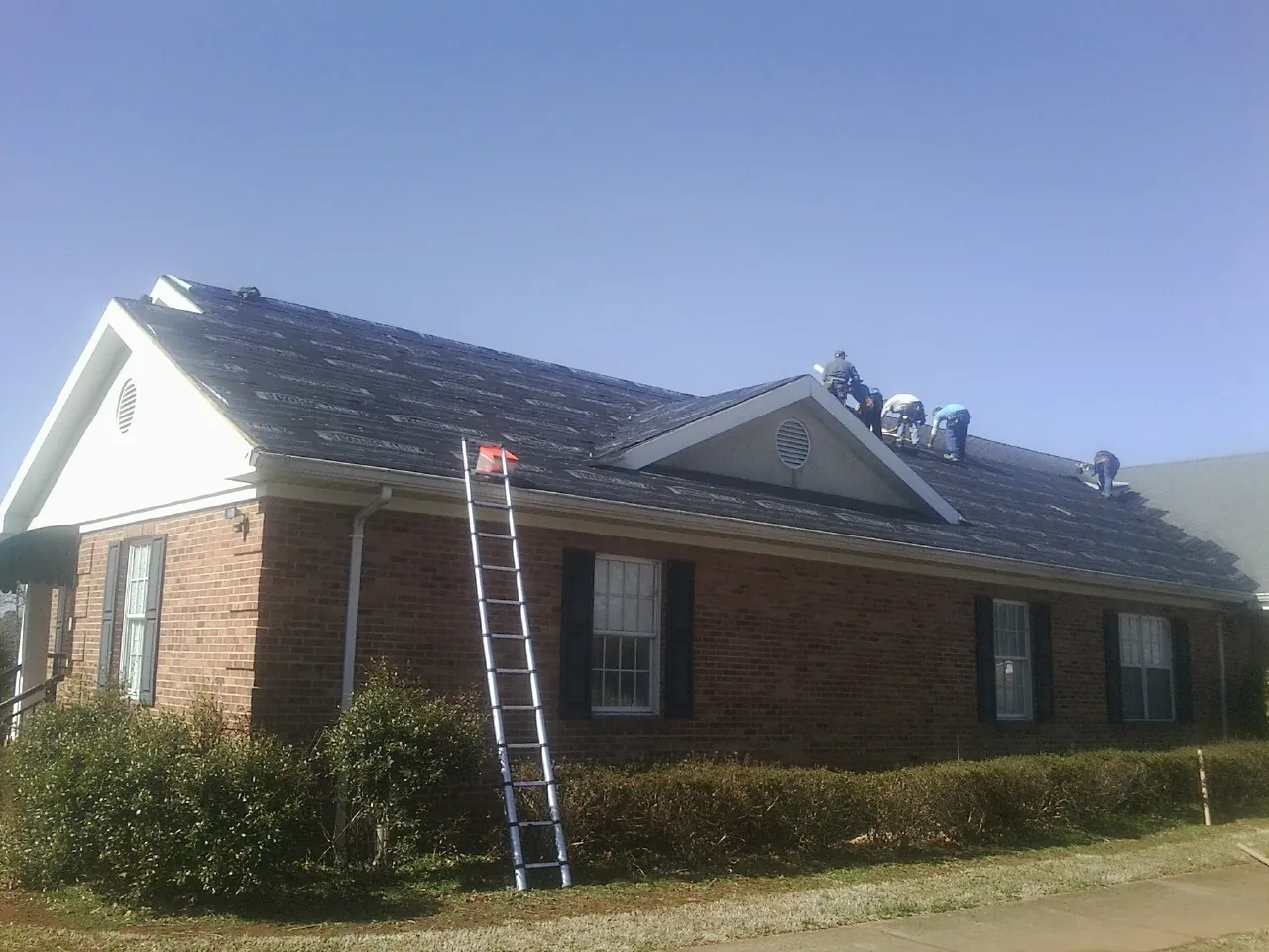 Crew tearing shingles off a brick ranch roof with a ladder set — Metal Roof Repair work by our crew in West Roxbury
