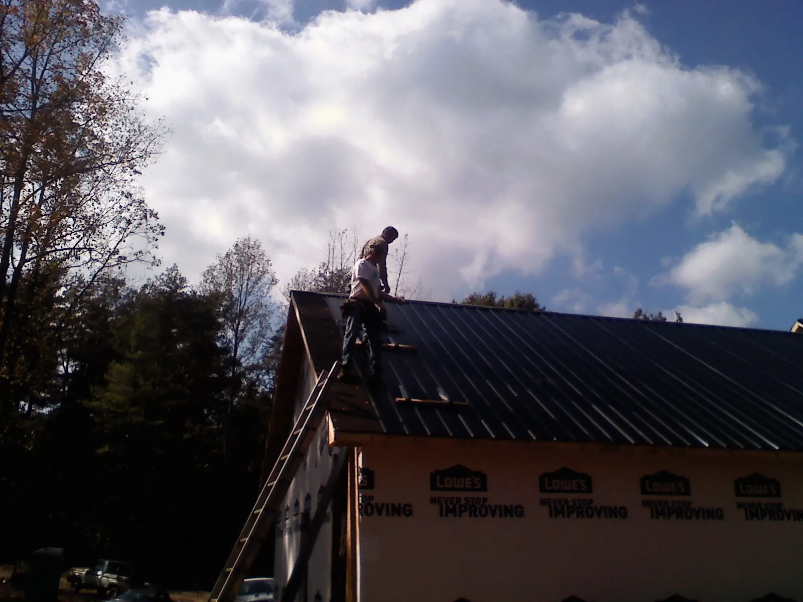 Roofer fastening dark metal panels high against a cloudy sky, from a Roof Inspection job in West Roxbury