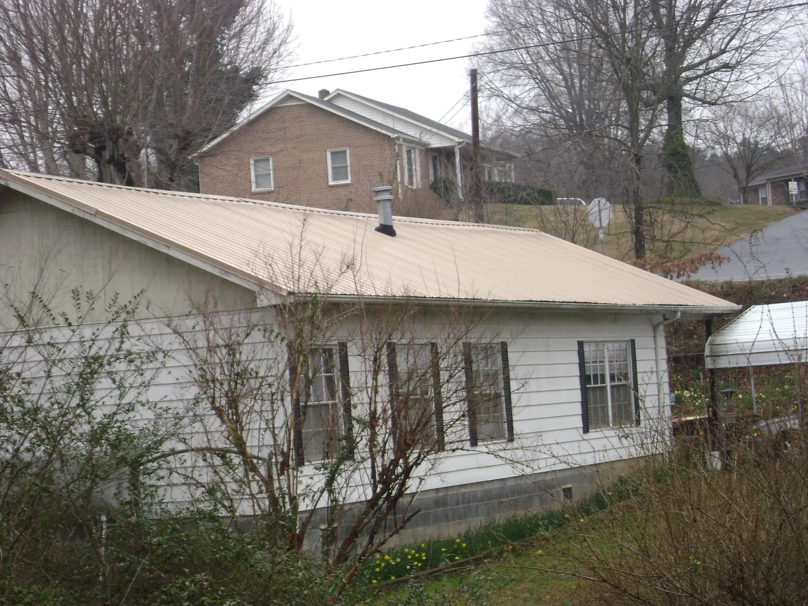 Tan metal roof on a white sided house set into a hillside — Commercial Roofing by Roofing Brothers in West Roxbury